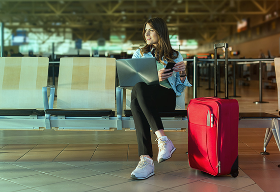 Passenger on smart phone and laptop sitting in airport terminal hall